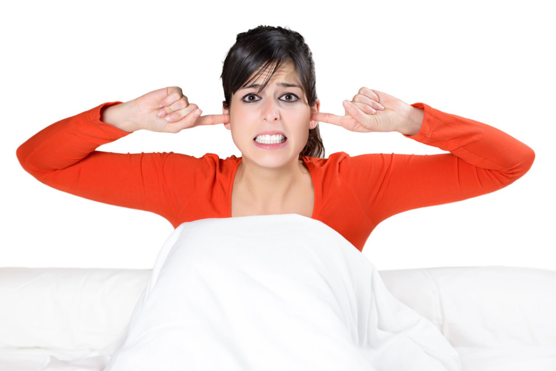 Femme stressée dans son lit, les doigts dans les oreilles à cause du bruit extérieur – illustration des nuisances sonores et de l'importance de l'isolation acoustique des fenêtres.